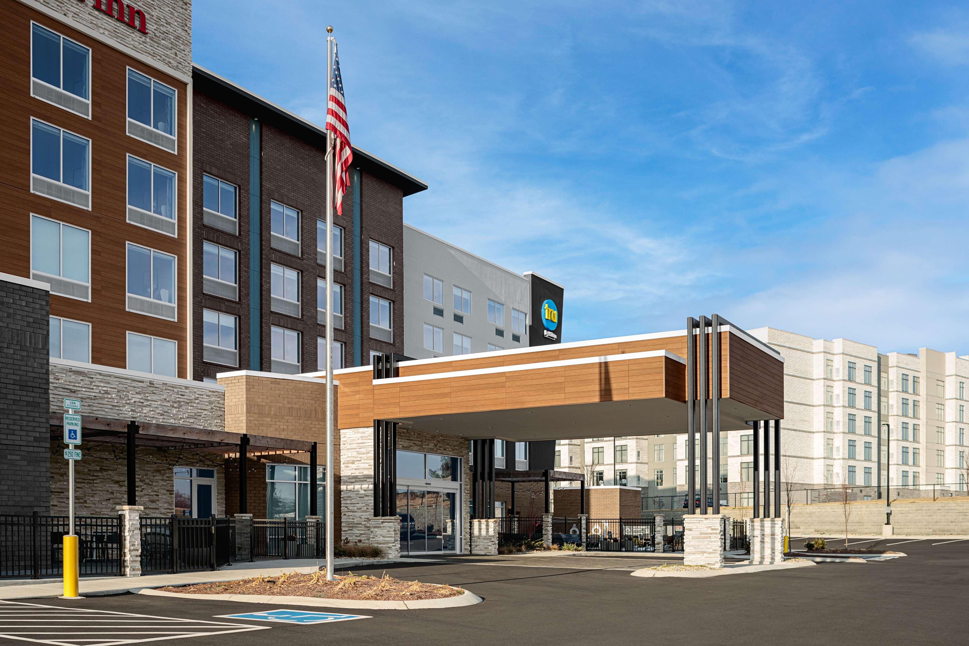 A modern hotel with a covered entrance, a flag, and a sign indicating amenities.