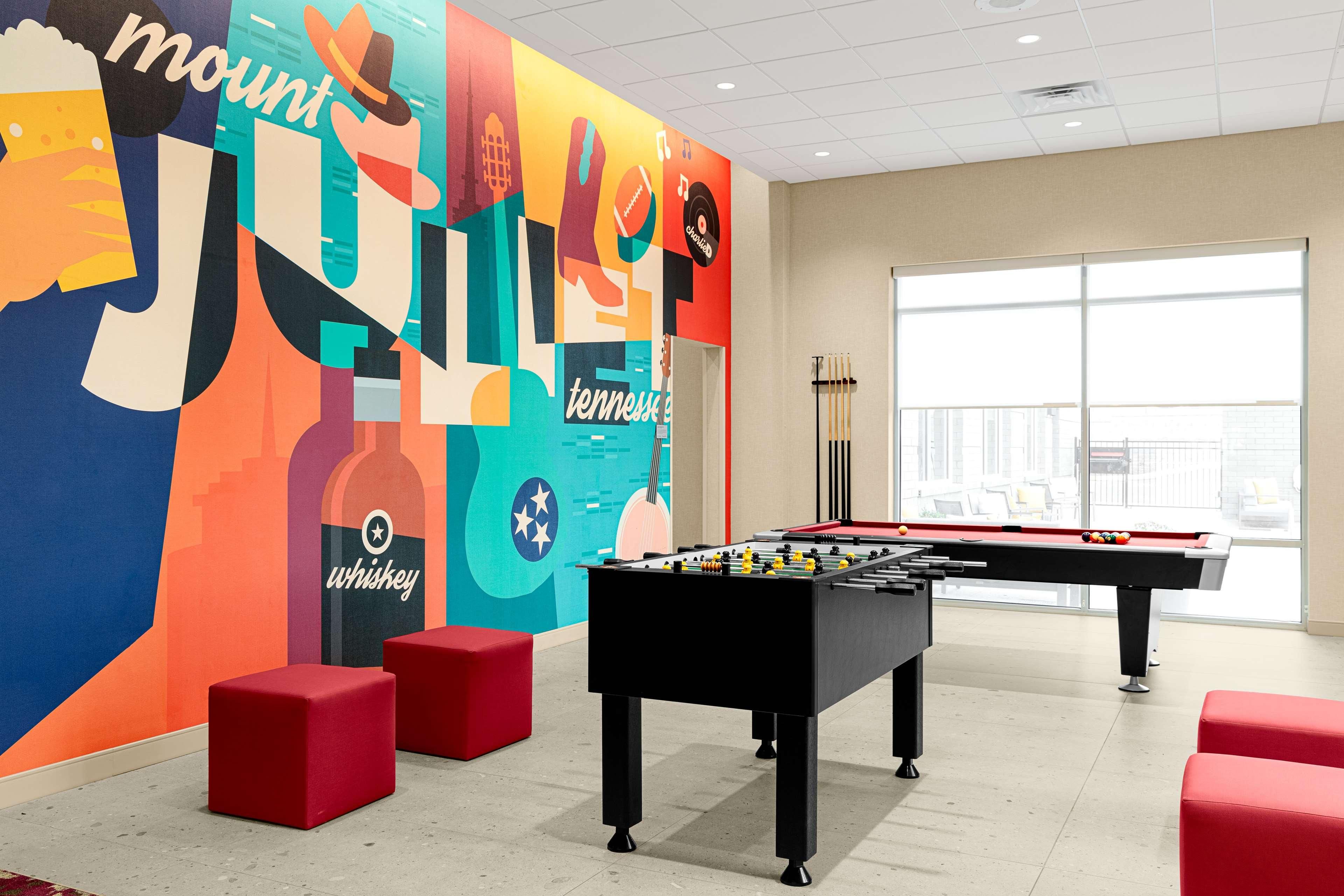 A room with a foosball table, red seating, and a colorful wall mural.