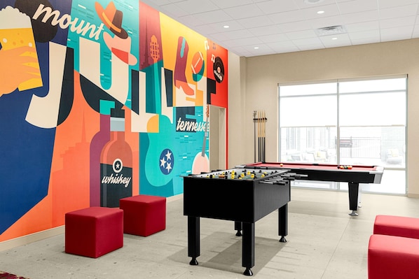 Una habitación con mesa de fútbol de mesa, asientos rojos y un colorido mural.
