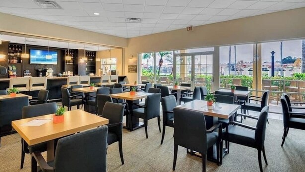 Un'ampia sala da pranzo interna con diversi tavoli e sedie, un'area bar con televisore, e ampie finestre che offrono vista sull'esterno.