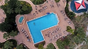 Vista aerea di una zona piscina con un motivo a scacchi intorno alla vasca, sedie a sdraio e un piccolo giardino circolare con una palma.
