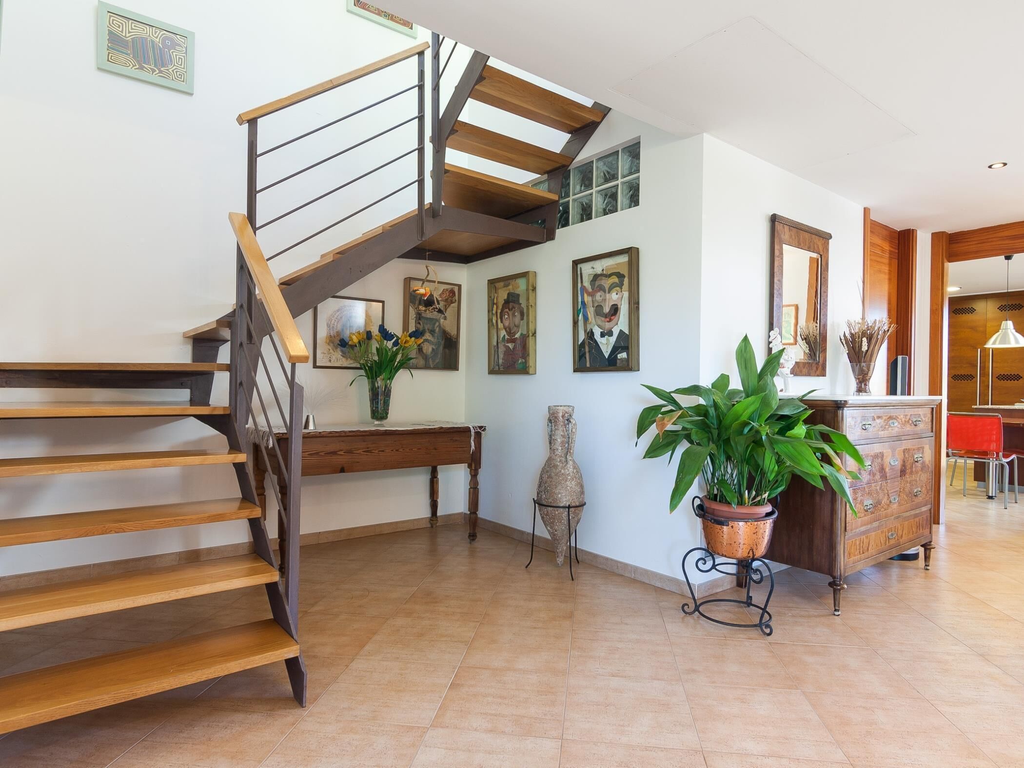 A spacious living area with a wooden staircase, a dining area, and a kitchen visible in the background.