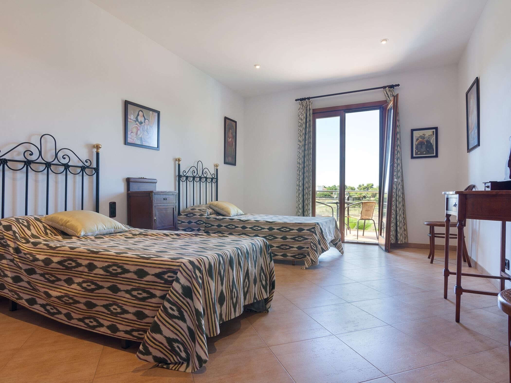 A bedroom with two beds, a desk, and a balcony.