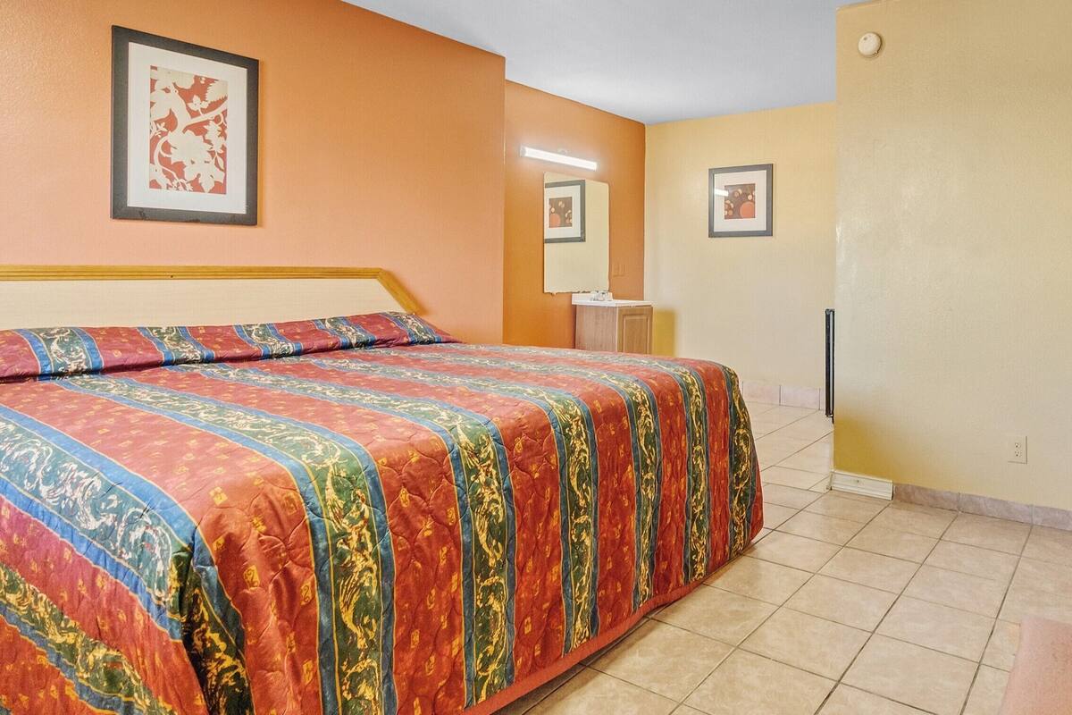 Un dormitorio con cama, mesita de noche, espejo y una pared decorada con cuadros.