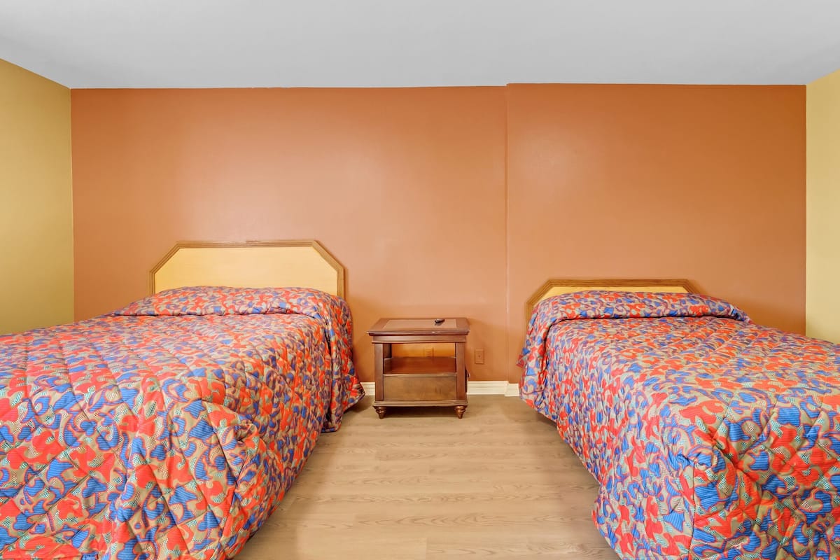 Una habitación con dos camas, una mesita de noche y suelo de madera.