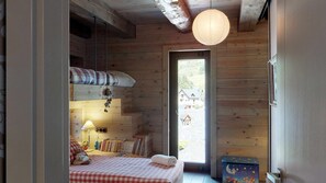 A cozy bedroom with a bed, bedside table, lamp, and a view of the outside.