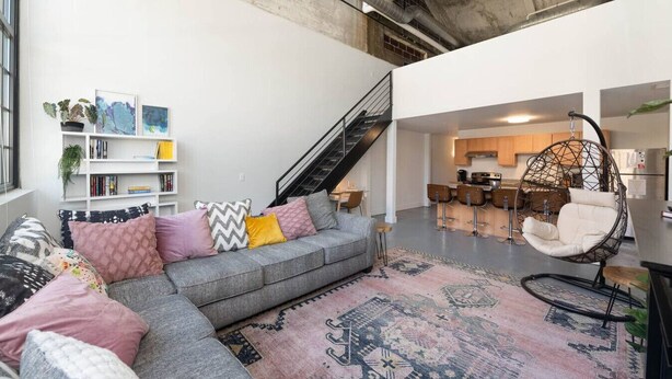 Ein zeitgemäßer Wohnbereich mit grauem Ecksofa, einem Hängesessel, einer Treppe und einer Küchenzeile.