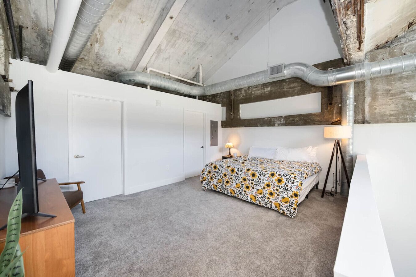 A bedroom with a bed, a desk, a chair, a lamp, and a television.