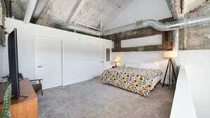 Ein Schlafzimmer mit einem Bett, einem Schreibtisch, einem Sessel, einer Lampe und einem Fernseher.