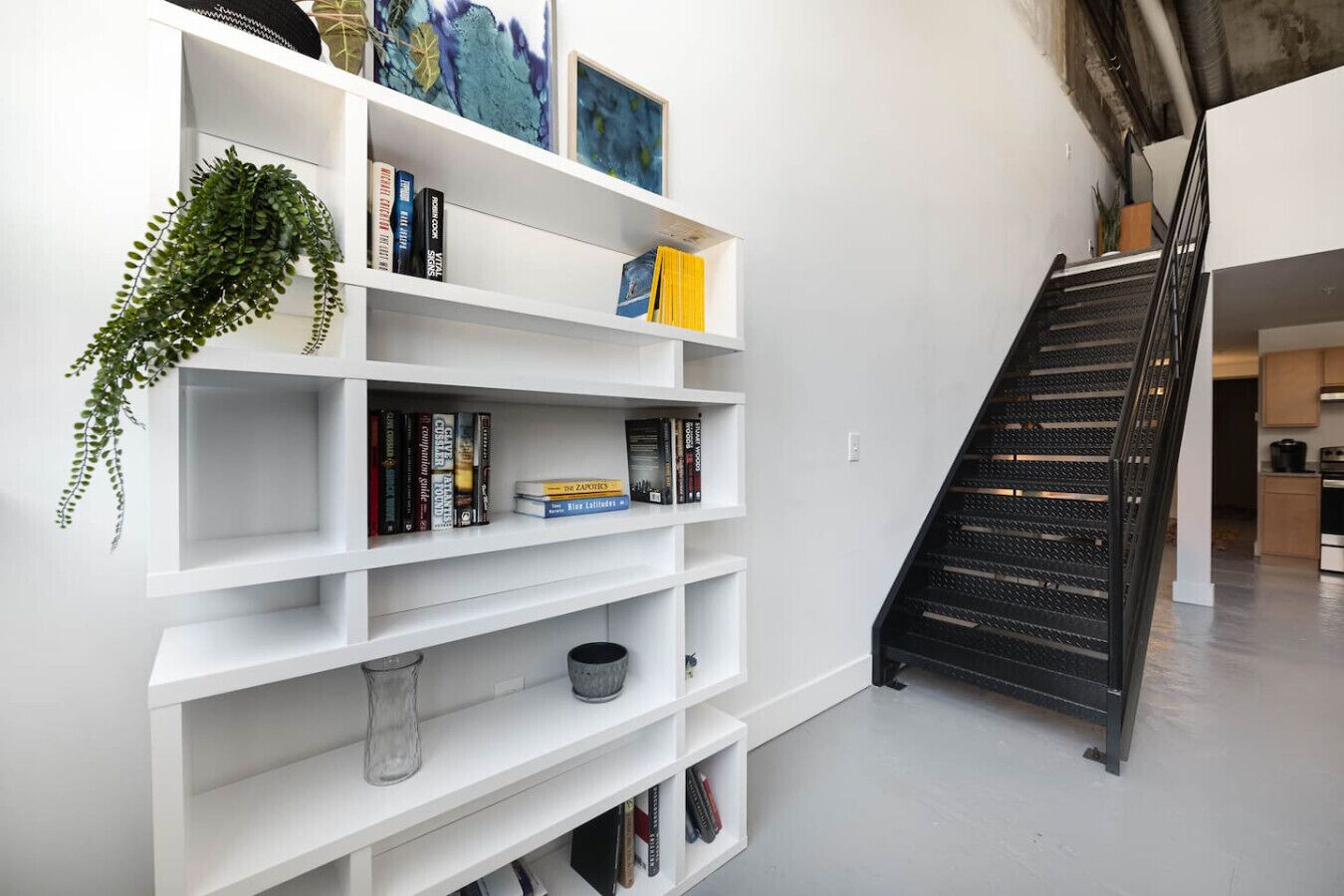 A modern interior with a white bookshelf, a staircase, and a kitchen area.