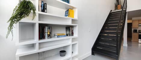 A modern interior with a white bookshelf, a staircase, and a kitchen area.