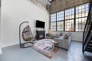 Een moderne woonkamer met een hangstoel, een open haard, een bank en grote ramen.