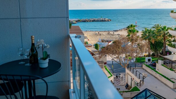 A balcony with a table and chairs, overlooking a beach with a rocky breakwater and palm trees. - Suitur apartment with pool in Marbella beach (Marbella)