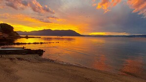 Una playa con mar tranquilo, una montaña distante y un cielo al atardecer.
