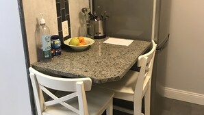 A compact kitchen with a granite countertop, white chairs, a small table, and a refrigerator. - Oceanview Apt - Steps to the Beach! (Long Beach)