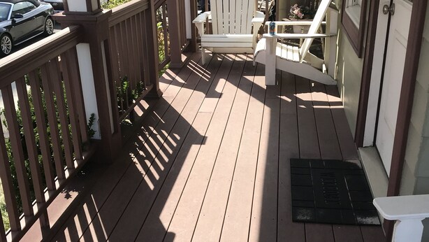 A wooden deck with a white chair and a small table, overlooking a street with parked cars and buildings. - Oceanview Apt - Steps to the Beach! (Long Beach)
