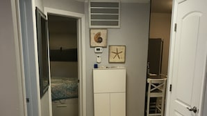 A hallway with a patterned rug, a white cabinet with a starfish decoration, and a door leading to a bedroom. - Oceanview Apt - Steps to the Beach! (Long Beach)
