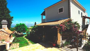 A two-story house with a tiled roof, a small balcony, and a garden with a pathway leading to a brick structure. - 4 Bed Villa Sleeps 9 - Pool, Pets, Garden, Parking (Supetar)