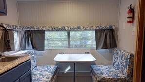 A compact RV kitchen with a sink, a table, and two bench seats with floral upholstery. - Secluded Camper with hot shower (Healy)