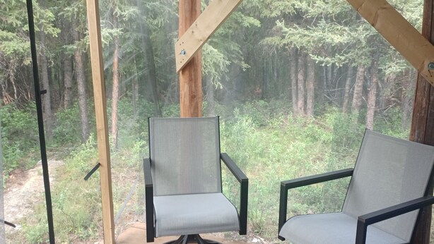 A wooden deck with two chairs and a glass door leading to a forested area. - Secluded Camper with hot shower (Healy)