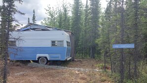 A blue and white RV parked in a forested area with a sign reading "Camp Seclusion." - Secluded Camper with hot shower (Healy)