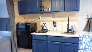 A compact kitchen with blue cabinets, a black refrigerator, a kettle, and a sink. - Secluded Camper with hot shower (Healy)