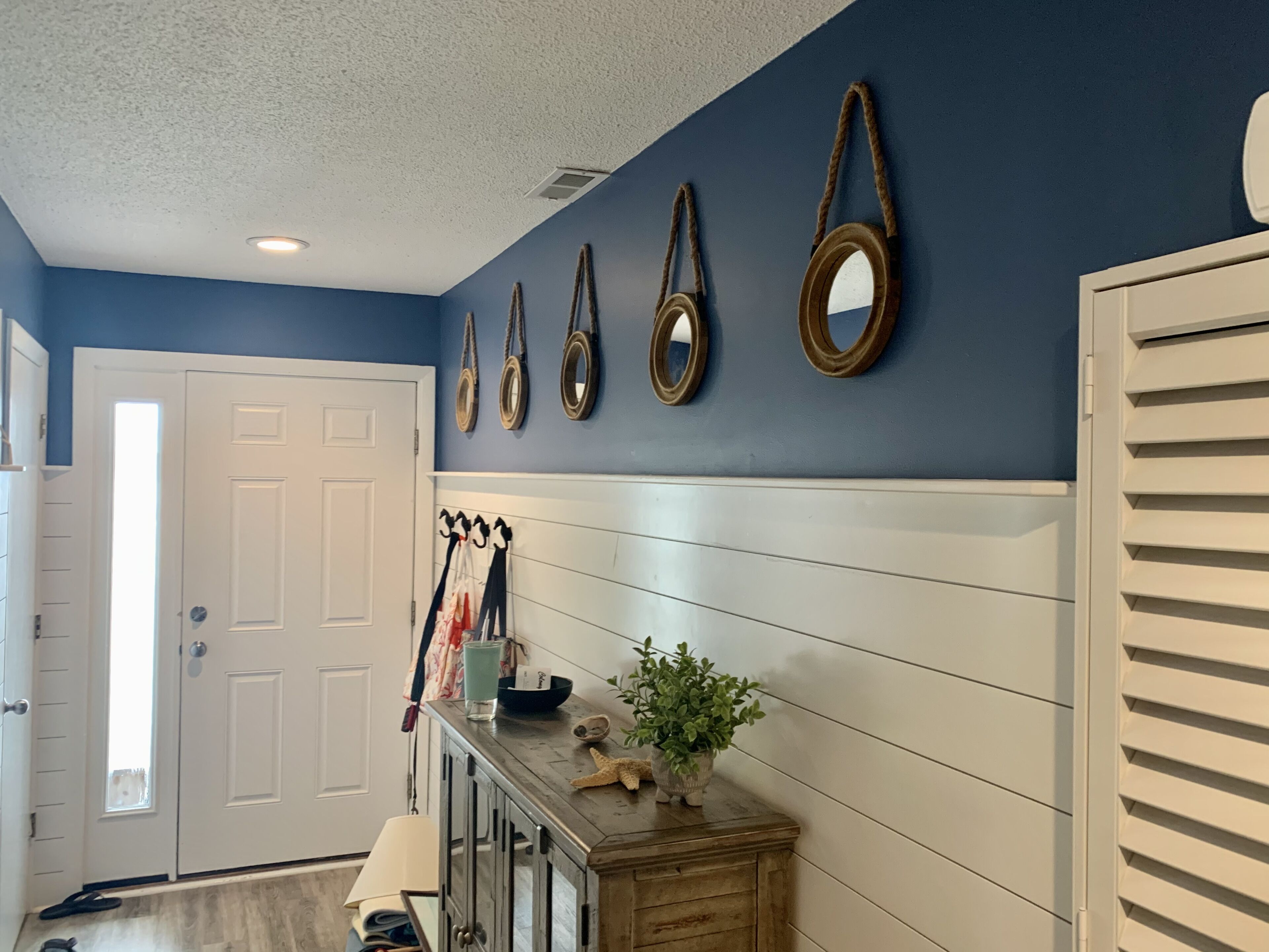 A hallway with a white door, a wooden console table with a plant and decorative items, and a row of wall-mounted mirrors.