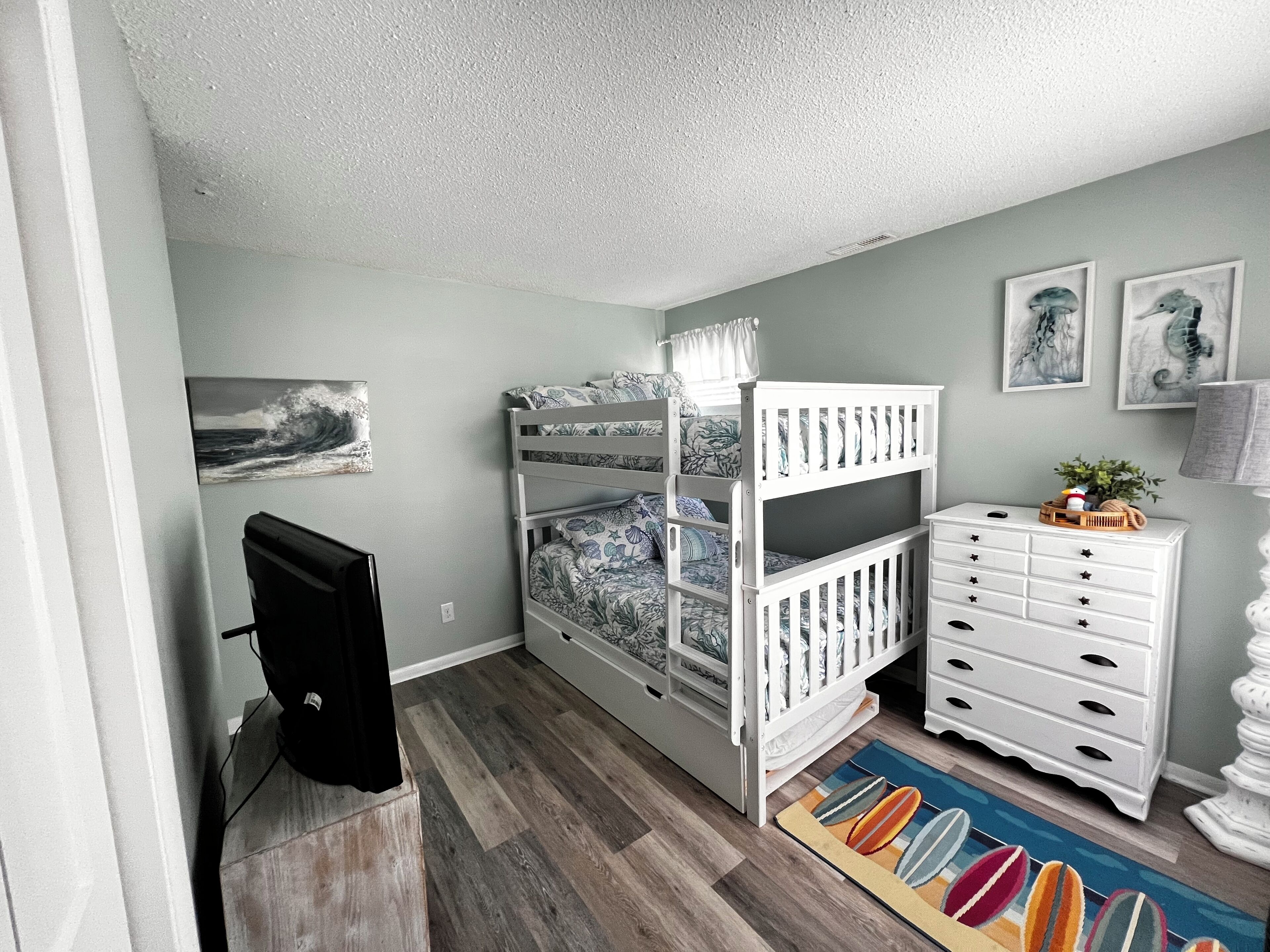 Une chambre d’enfant avec des lits superposés, une commode, un tapis et des œuvres d’art accrochées aux murs.