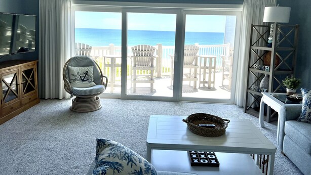 A living room with a view of the ocean, a white armchair, a coffee table, and a TV on a wooden cabinet.