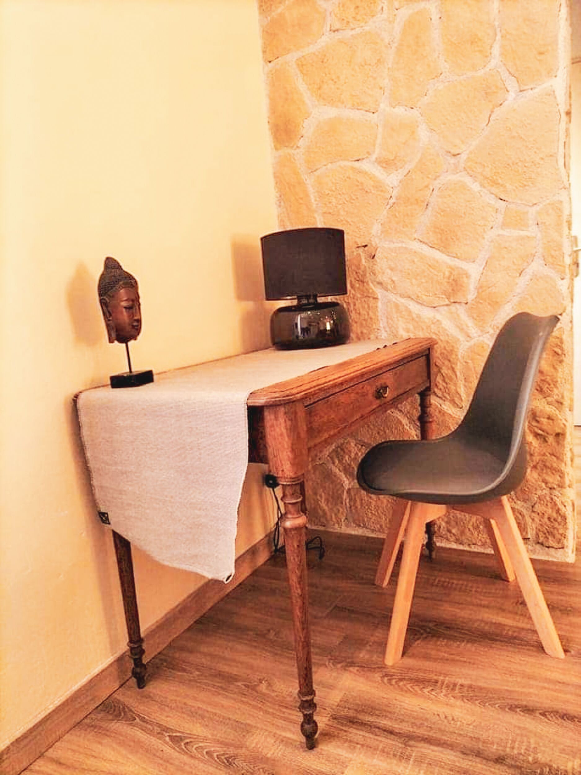 A corner room with a wooden desk, a black chair, a stone wall, and a small Buddha statue.