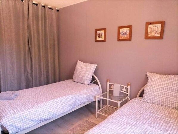 Un dormitorio con dos camas individuales, una mesita de noche de madera y una estantería en la pared.