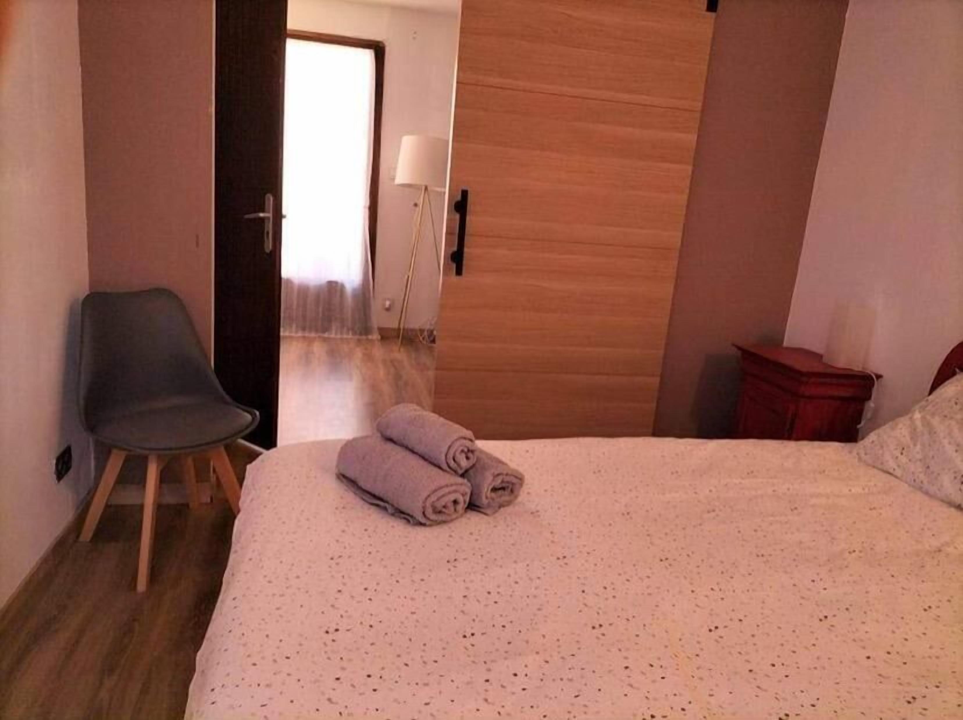 A hotel room with a bed, a chair, a wooden door, and a lamp.