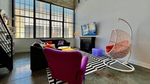 A modern living room with a sofa, a chair, a hanging egg chair, a flat-screen TV, and a fireplace. - 5109 Peters Cartridge Factory · ✪Kings Island Loft w/ Brewery, River, Bike trails✪ (Maineville)