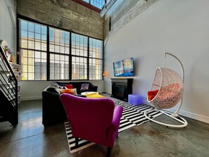 Een moderne woonkamer met een bank, een fauteuil, een hangstoel, een flatscreen televisie en een open haard.