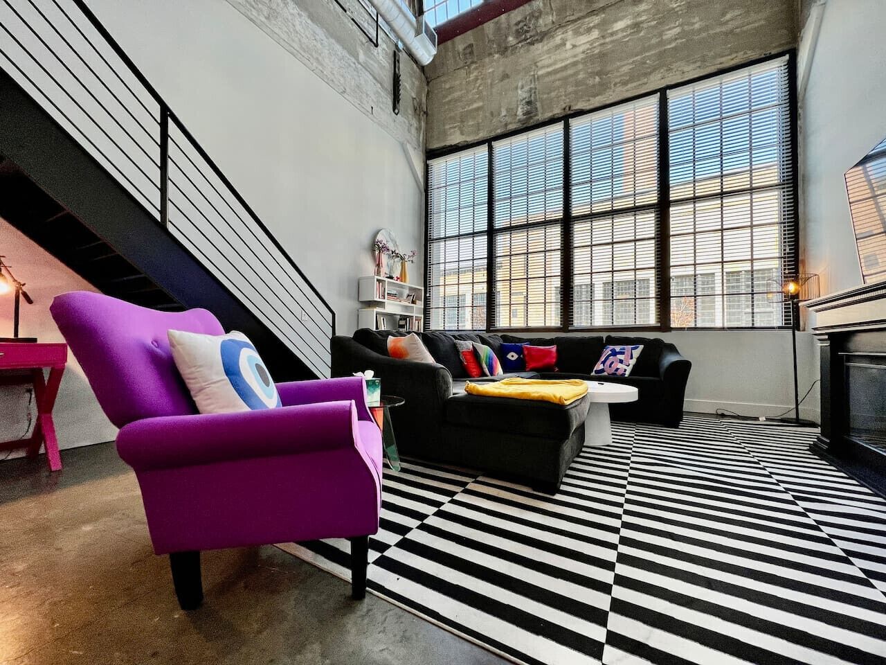 Un salon moderne avec un sol à carreaux noirs et blancs, un canapé noir agrémenté de coussins colorés et un fauteuil violet.