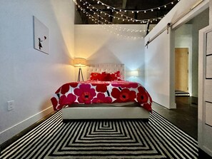 A bedroom with a bed, a lamp, and a wall-mounted picture.
