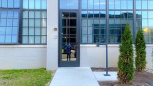 A modern building with a large glass entrance, a concrete pathway leading to the door, and two small evergreen trees. - 5109 Peters Cartridge Factory · ✪Kings Island Loft w/ Brewery, River, Bike trails✪ (Maineville)