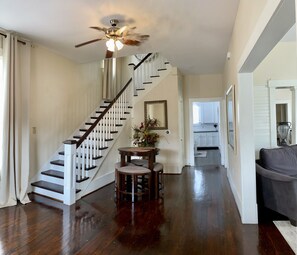 A spacious living area with a wooden staircase, a ceiling fan, and a dining table with chairs.