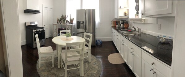 A compact kitchen with white cabinets, a black countertop, a stove, a refrigerator, and a dining area with a table and chairs.