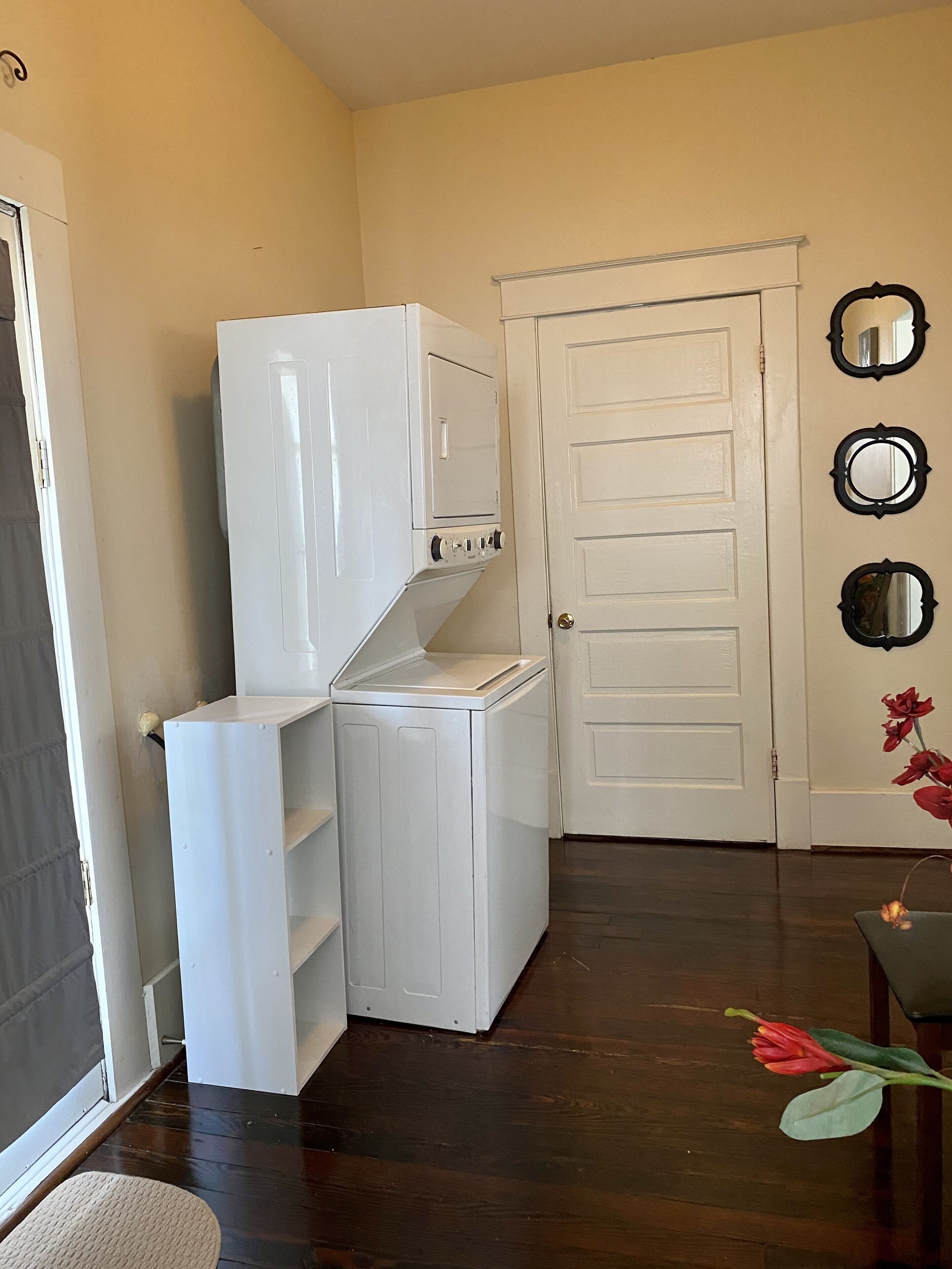 A laundry room with stacked washer and dryer, a door, and wall-mounted mirrors.