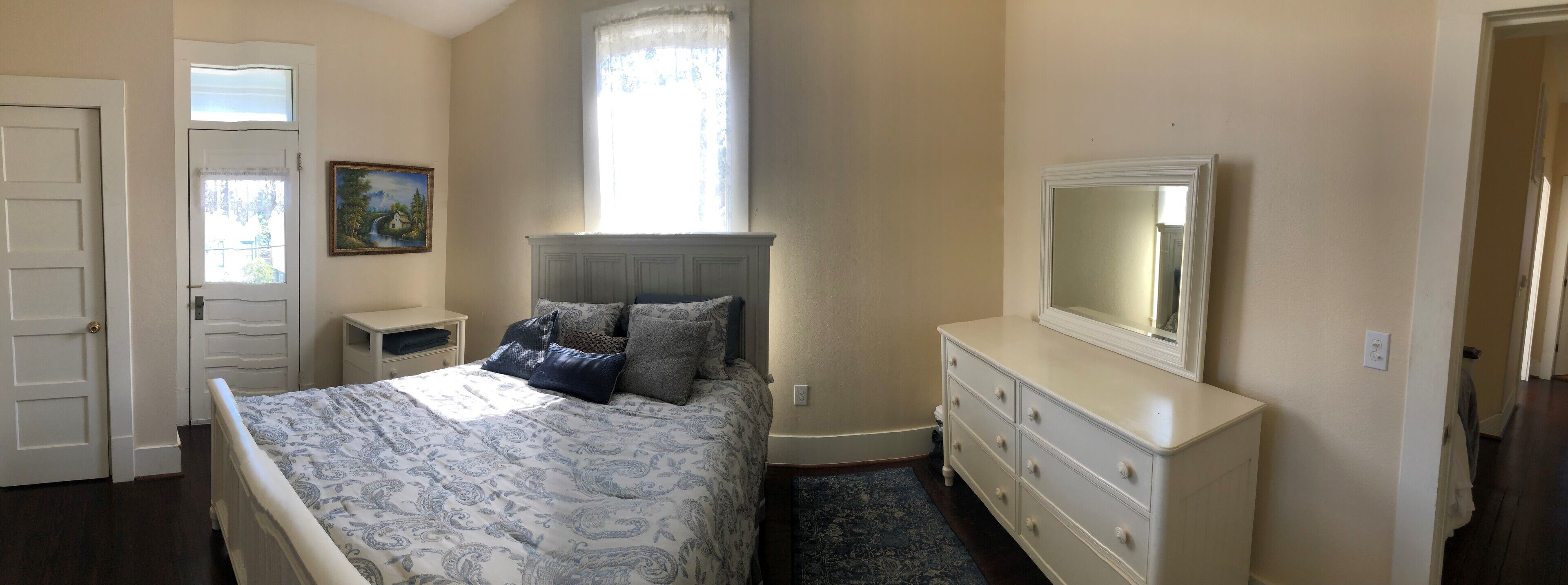 Une chambre à coucher comprenant un lit, une commode, une table de chevet, une fenêtre avec vue et un tableau accroché au mur.