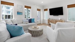 Un salon moderne comprenant un canapé, des fauteuils, une table basse et un téléviseur à écran plat fixé au mur.