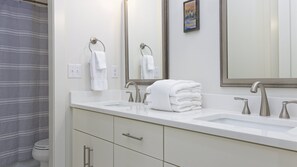 A modern bathroom with a white sink, two faucets, a mirror, and a toilet. - Beach Side Home, Steps from the Sand. Ocean Edge 03 | A Wave From It All by Kaiser Vacation Rentals (Orange Beach)