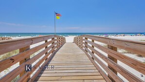 Ein Holzsteg führt zu einem Strand mit einer Flagge.