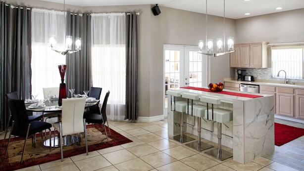 Cocina moderna con una isla de mármol, comedor con alfombra roja y vistas al salón a través de un ventanal.