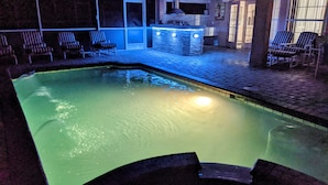 Una piscina interior con borde de piedra, sillones de descanso y zona de bar con iluminación azul.