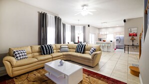 Una sala de estar moderna con un sofá seccional color beige, una mesa de centro blanca y una alfombra estampada.