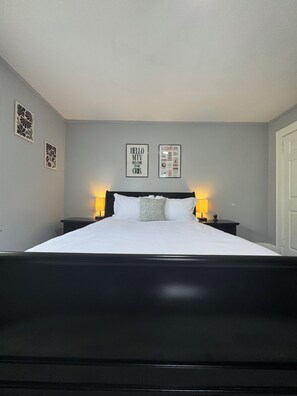 Une chambre à coucher avec un cadre de lit noir, deux tables de chevet avec des lampes et deux tableaux encadrés accrochés au mur.
