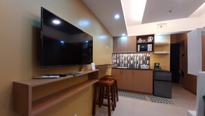 Una cocina moderna con televisión de pantalla plana, barra de madera, taburetes y microondas.