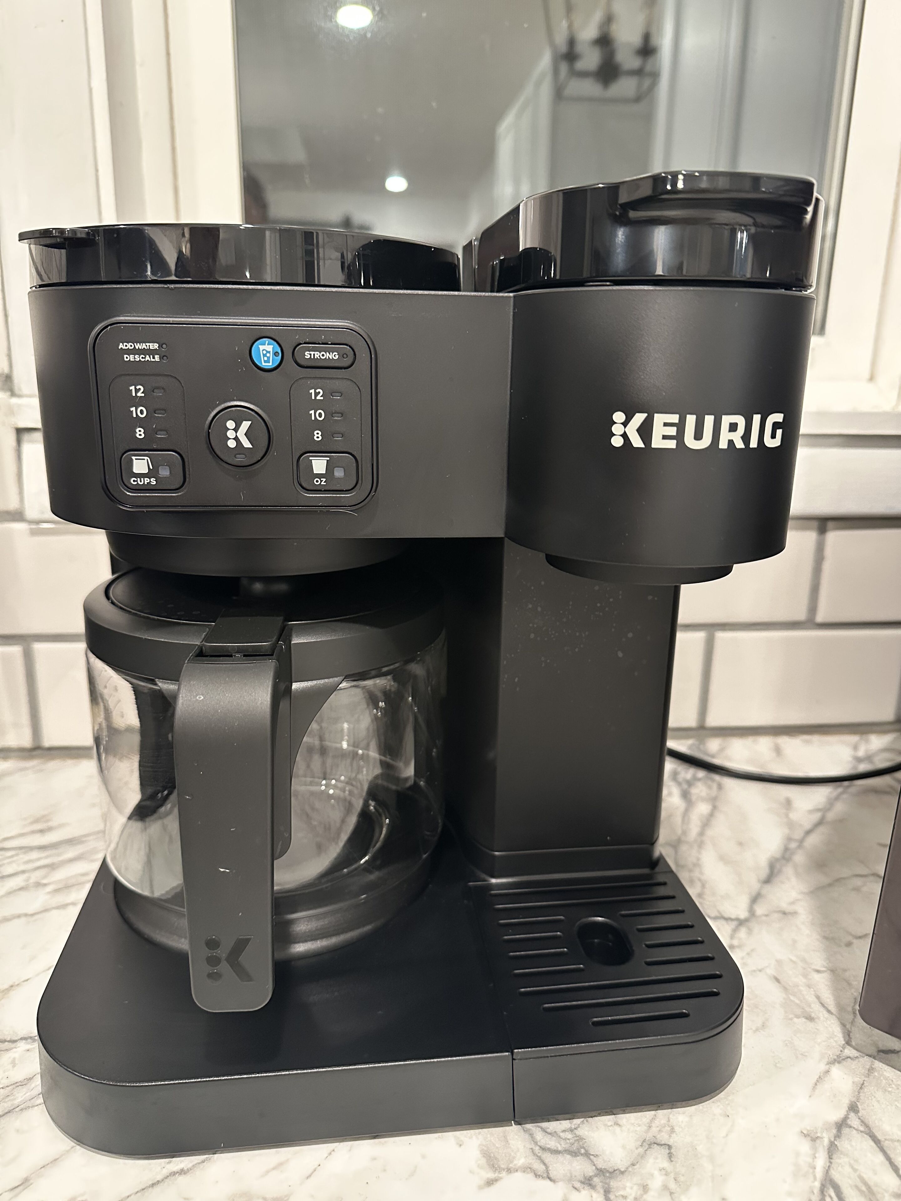 A black Keurig coffee maker with a glass carafe and a water reservoir, placed on a marble countertop.